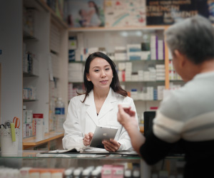 An Asian femail pharmacist assists an older Asian male customer
