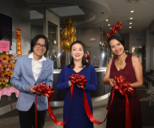 Three East Asians prepare to cut the ceremonial ribbon at the grand opening of their business.